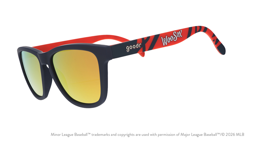 Three-quarter angle view of shades. Dark blue frames w/ a red pattern, WooSox on temples + amber reflective lenses.