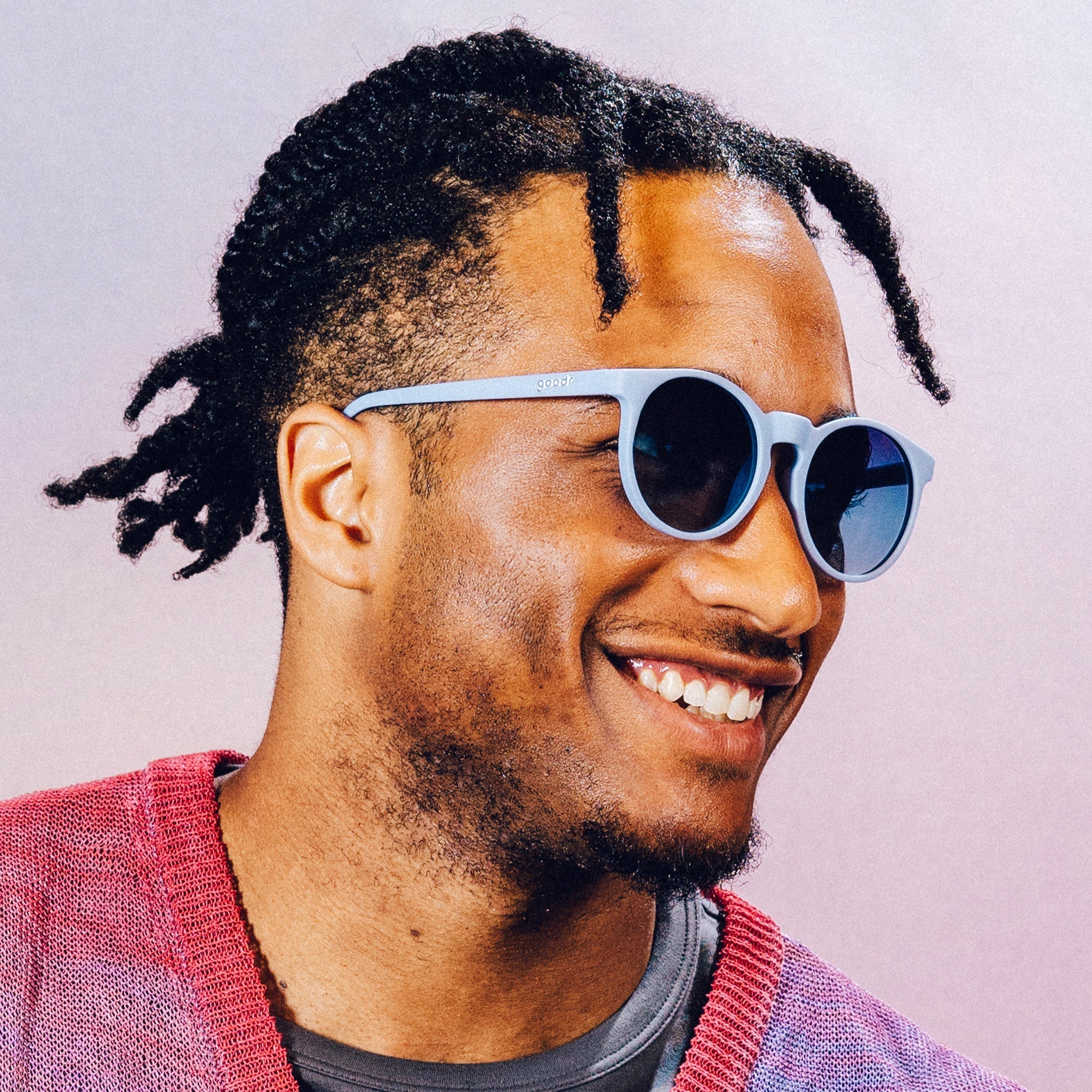 Side profile of a man smiling and wearing light blue circular sunglasses with dark blue gradient lenses.